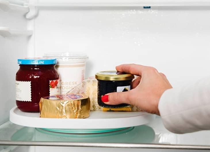 A person gets a small jam bottle from a lazy susan, with greek yoghurt, strawberry jam, and butter on it