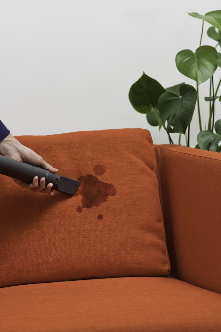 A person vacuums an orange upholstery to help fade the stain
