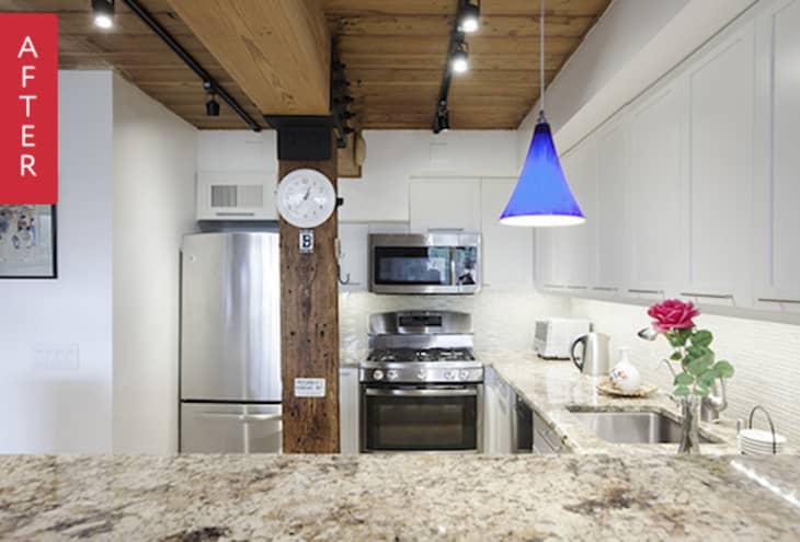 A modern white kitchen with a blue hanging pendant light and track lights on the ceiling
