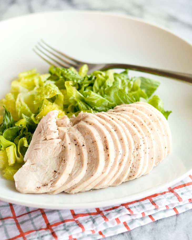 Plate of poached chicken, sliced and fanned out, with salad greens