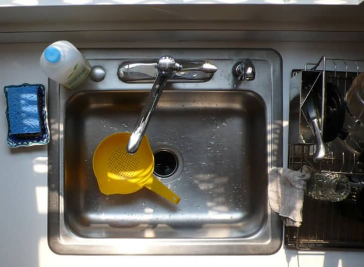 An aerial shot of a stainless steel sink with cleaning products and a yellow strainer