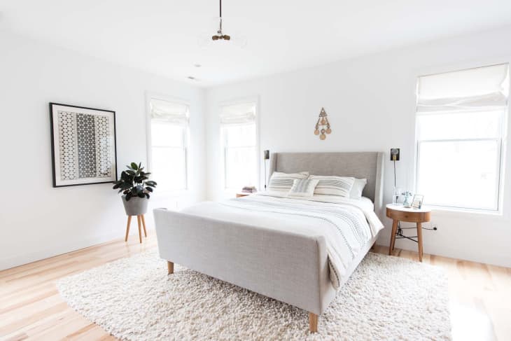 A bed with a grey fabric headboard on top of a beige shag rug.