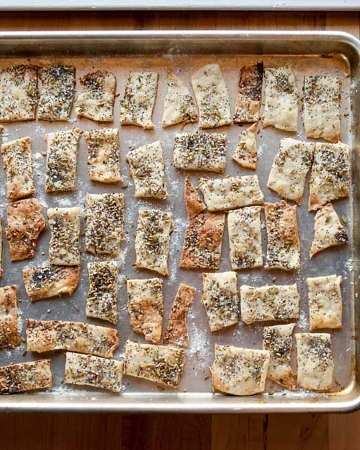 Homemade crackers, topped with fennel seeds, sesame seeds, and poppy seeds, on a baking sheet