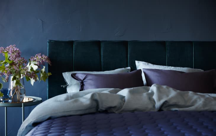 A blue upholstered headboard paired with purple bedding.