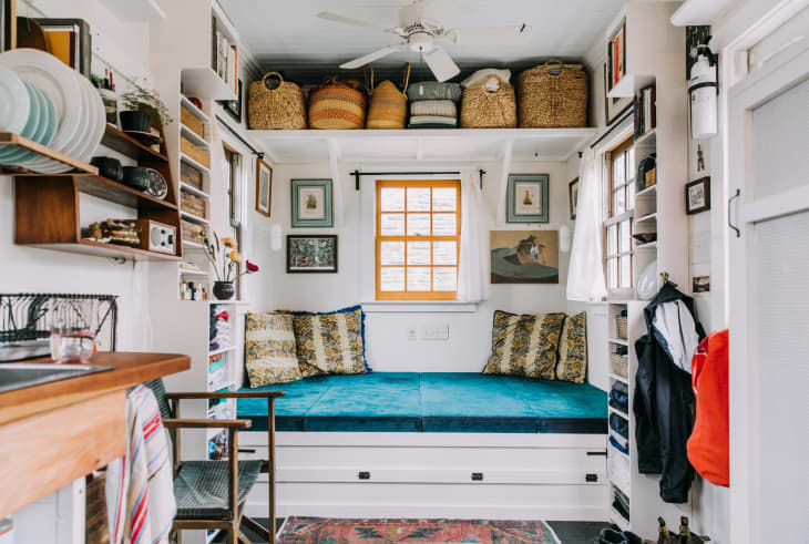 A tiny house with a built-in daybed and lots of storage solutions, including a shelf full of baskets