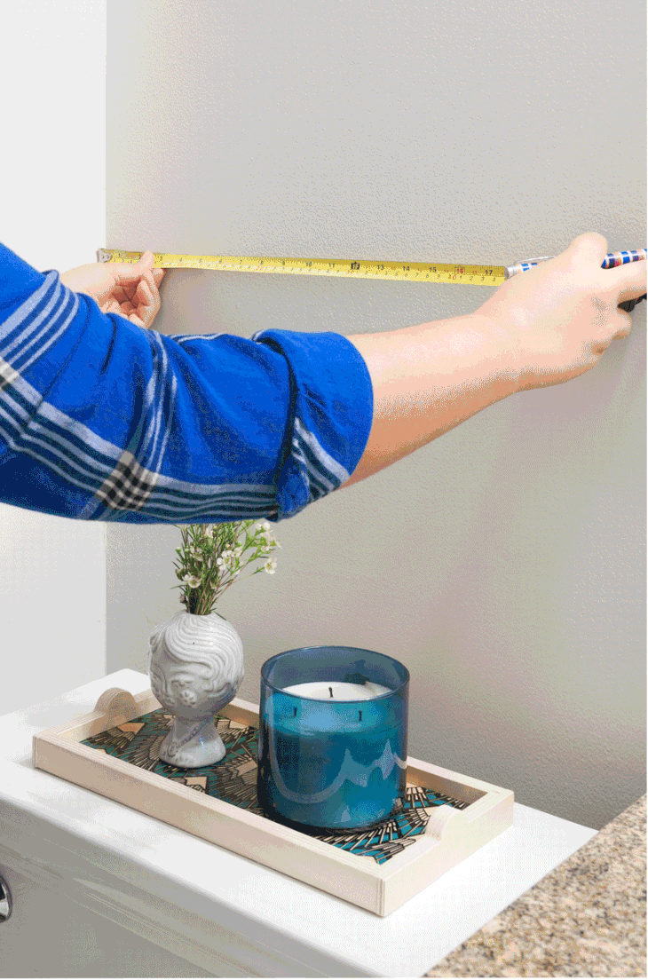 a man using a tape measure to install a shelving unit above the toilet
