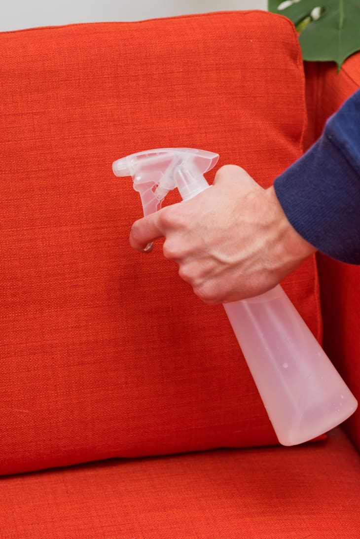 A man positions his fingers and prepares to use a spray bottle on the orange upholstery fabric