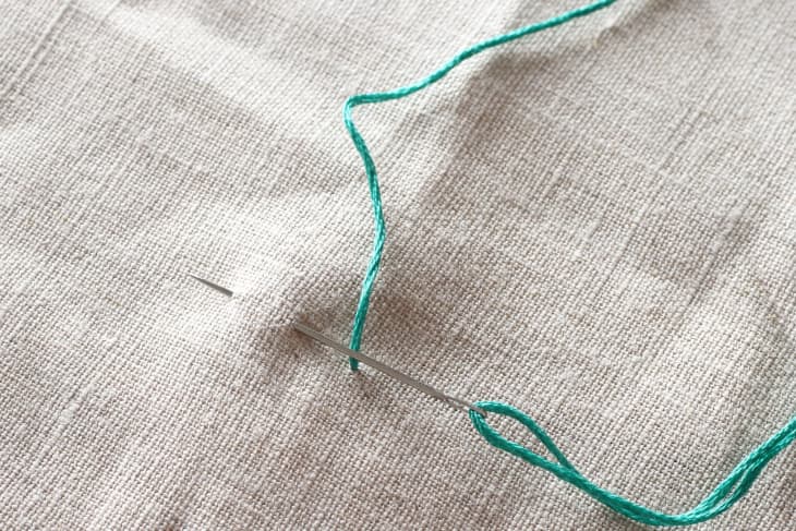 Needle piercing through canvas material with green thread