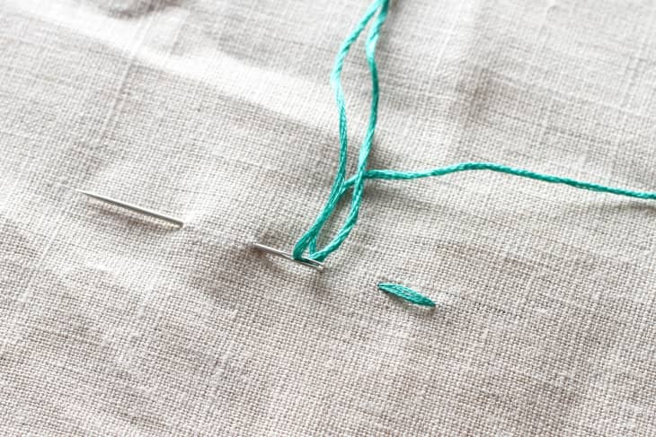 needle piercing through canvas material again in a straight line with green thread