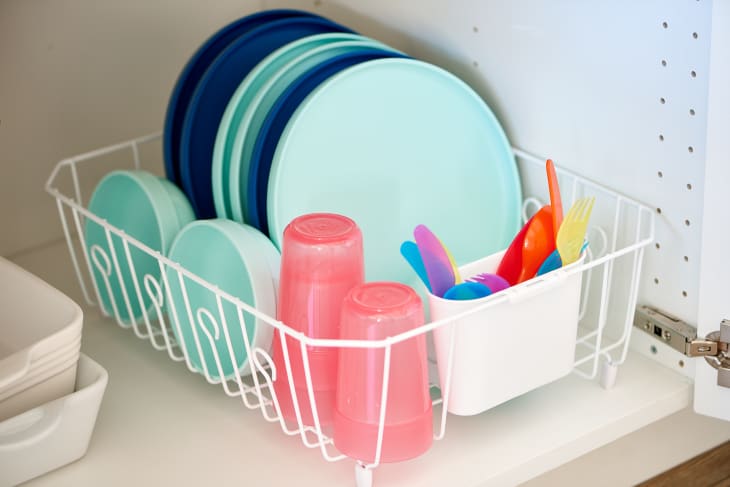 A dish rack holds kids' blue and green plates, bowls, pink plastic cups, and utensils