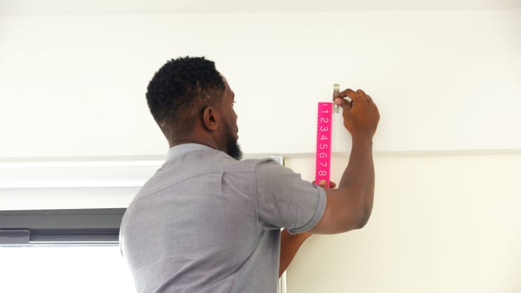 A Black man measuring where to hang his curtain rod