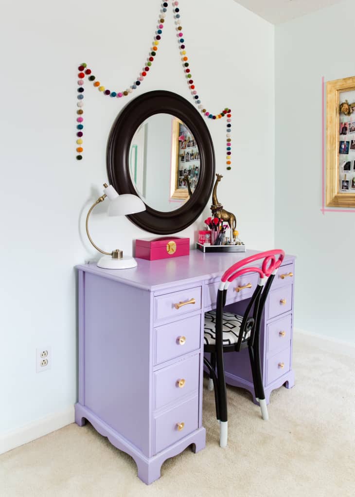 A purple desk with a mirror above and a colorful garland strung