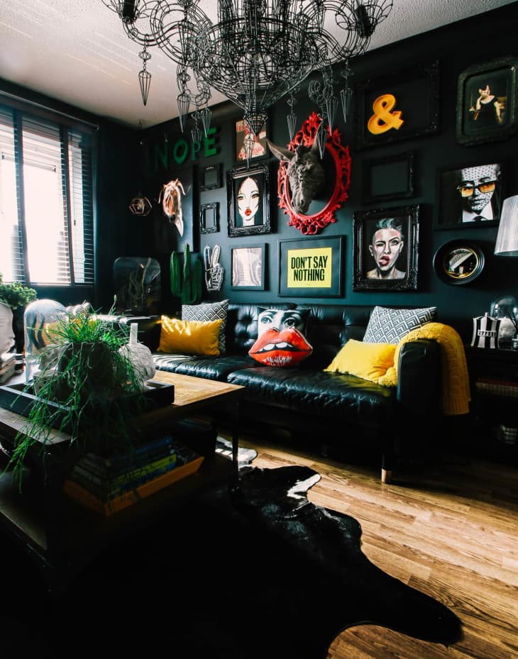 A living room painted in a dark color with a gallery-style wall covered in art in frames painted the same color as the wall