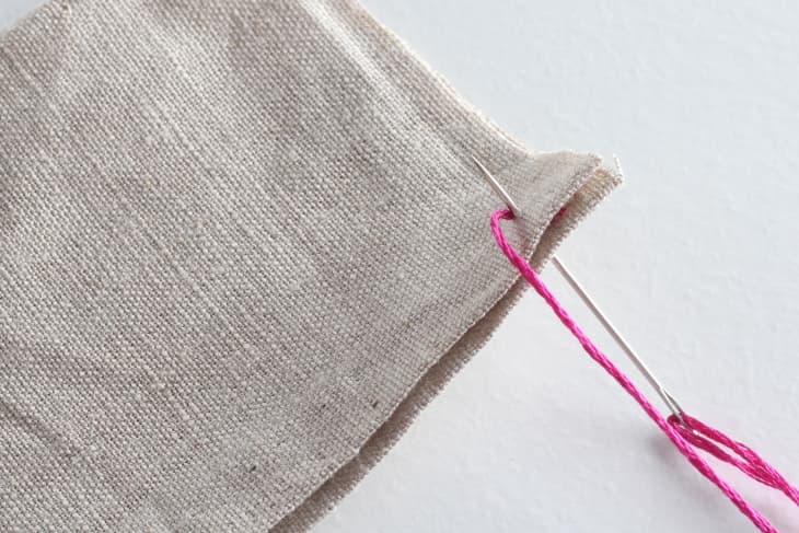 needle going through both ends of canvas with pink thread