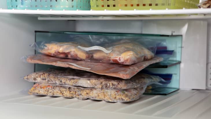 Different foods in a plastic bag are turned on their side and they are stashed in the corner of a freezer