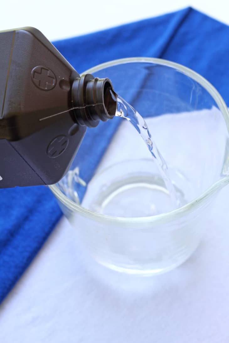 A bottle of hydrogen peroxide is being poured into an empty cup