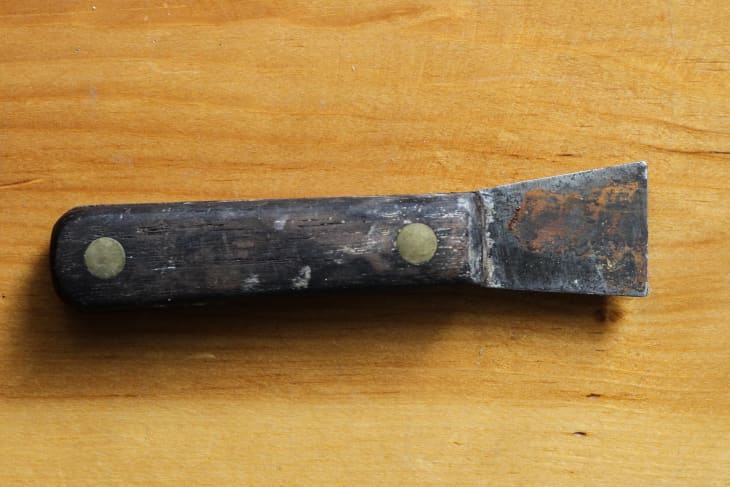 a rusted metal scraper with a wooden handle on a table