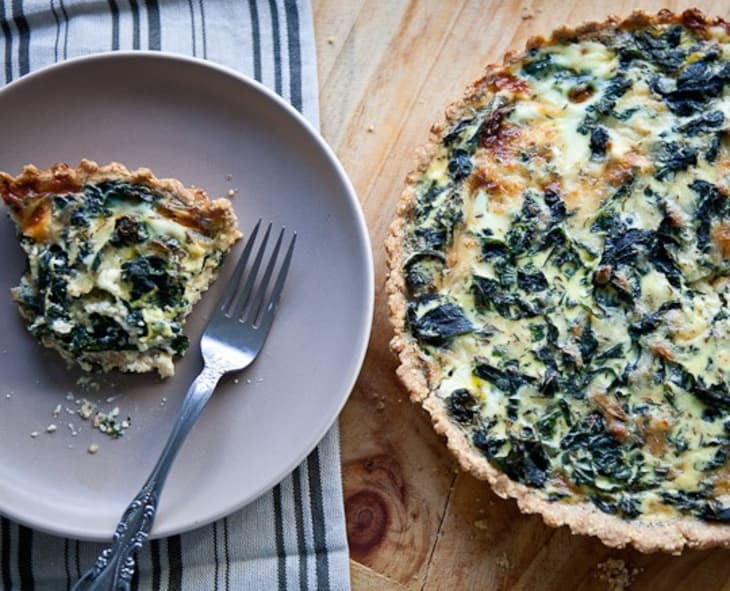 A piece of spinach quiche on a plate next to a spinach quiche in a pie dish