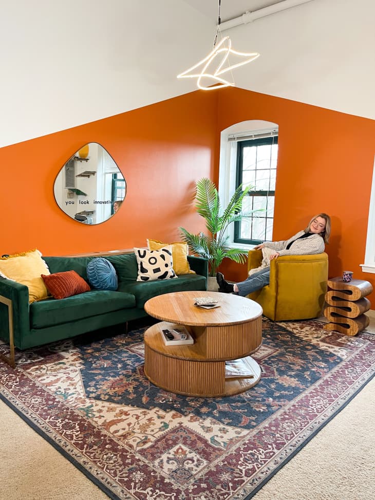 Spacious living room colorful orange wall decal and green velvet sofa and neon hanging pendant light.