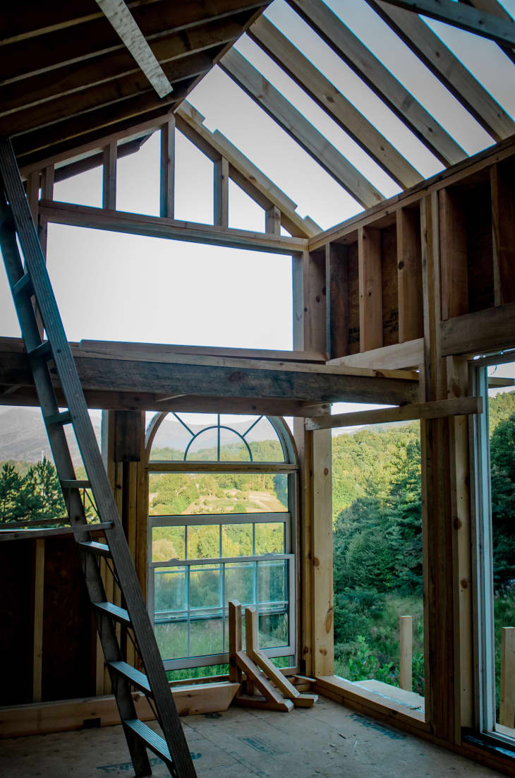 Interior of a building in progress with high ceilings, slanted wood beams, large arched window