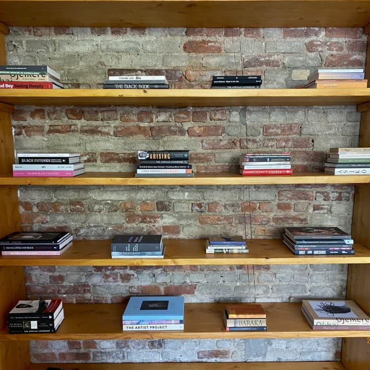Bookshelf designed by Stephanie Baptist. Wood shelves against brick wall, with stacks of books