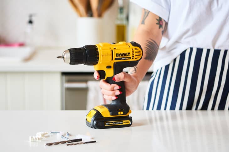 Girl holding a DeWALT power drill on the table next to screws