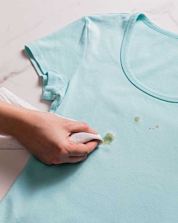 Blotting at an oil stain on a blue t-shirt