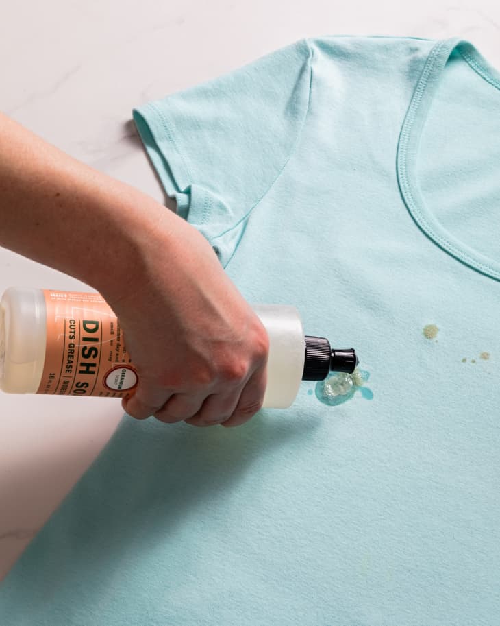 Applying dish soap to an oil stain on a blue t-shirt