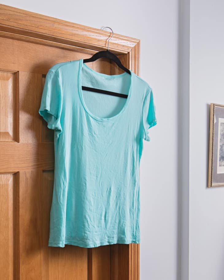 A freshly washed and treated t-shirt on a clothes hanger, hanging from an interior door's molding to air dry