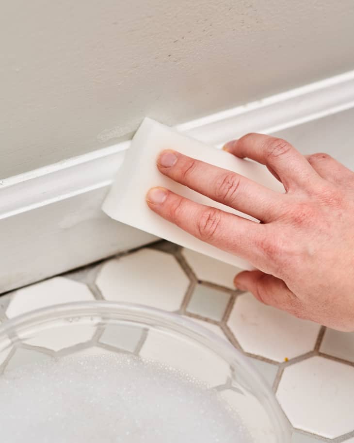 person wiping baseboards with magic eraser