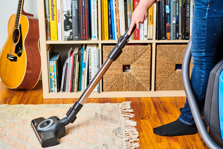 vacuuming rug in front of bookcase