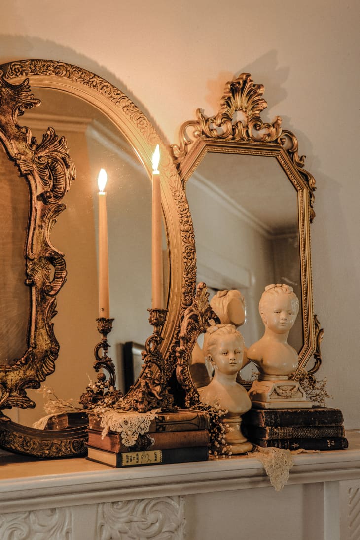 Fireplace mantle decorated with antique mirrors, old books, busts, and candles
