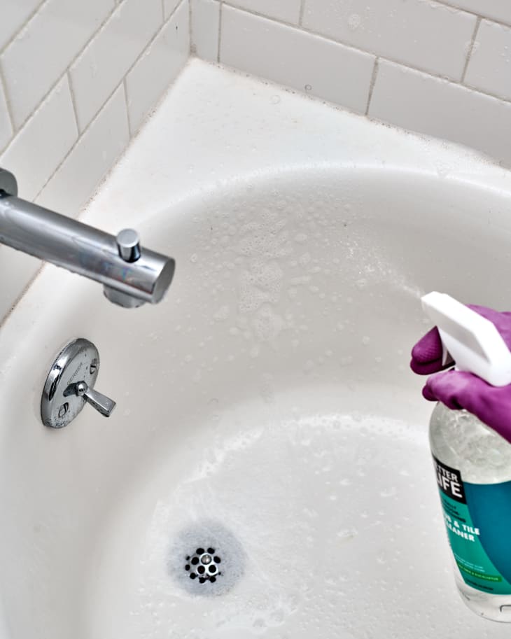 Spraying cleaner on the tub wearing dish gloves