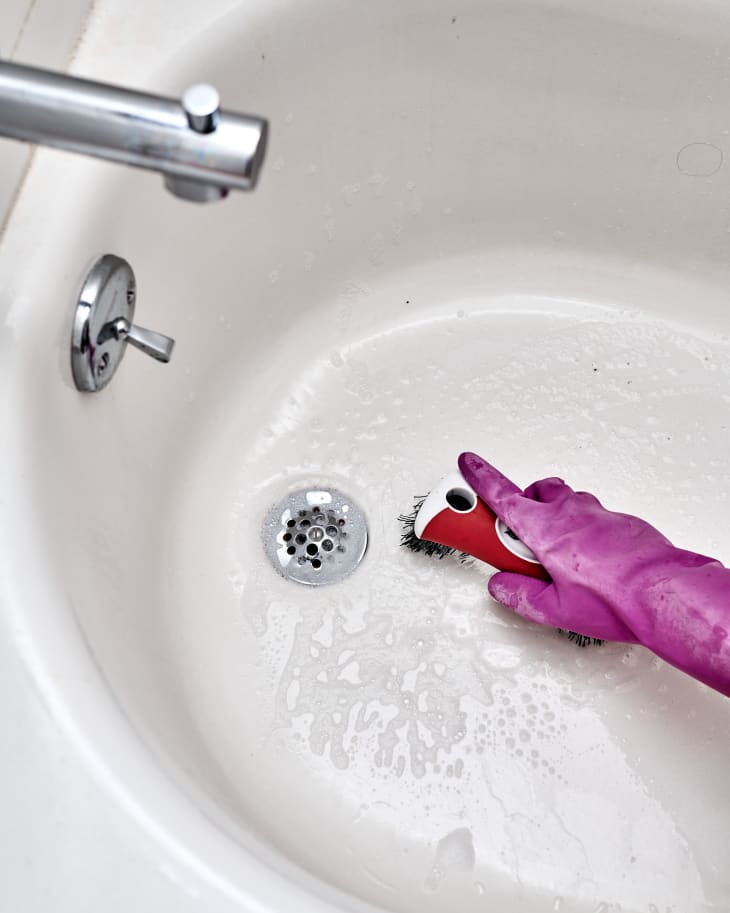 Scrubbing bottom of the tub with a sturdy brush wearing dish gloves