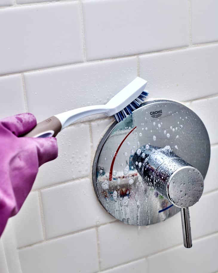 Scrubbing shower fixture with scrub brush to remove any buildup wearing dish  gloves