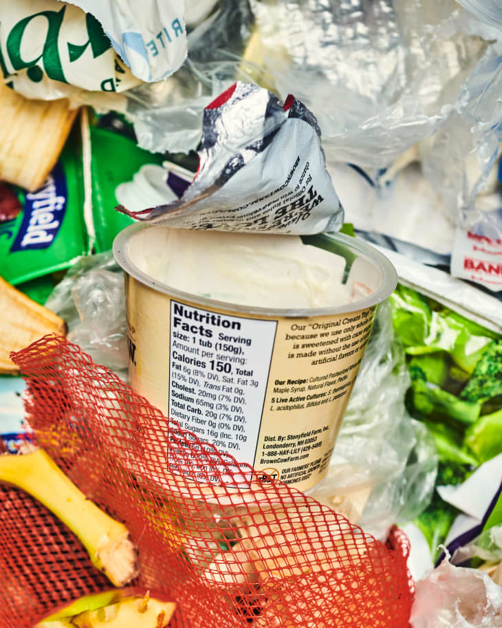 close up of trash in a bin showing old yogurt container, banana peel, milk carton, plastic, and other waste