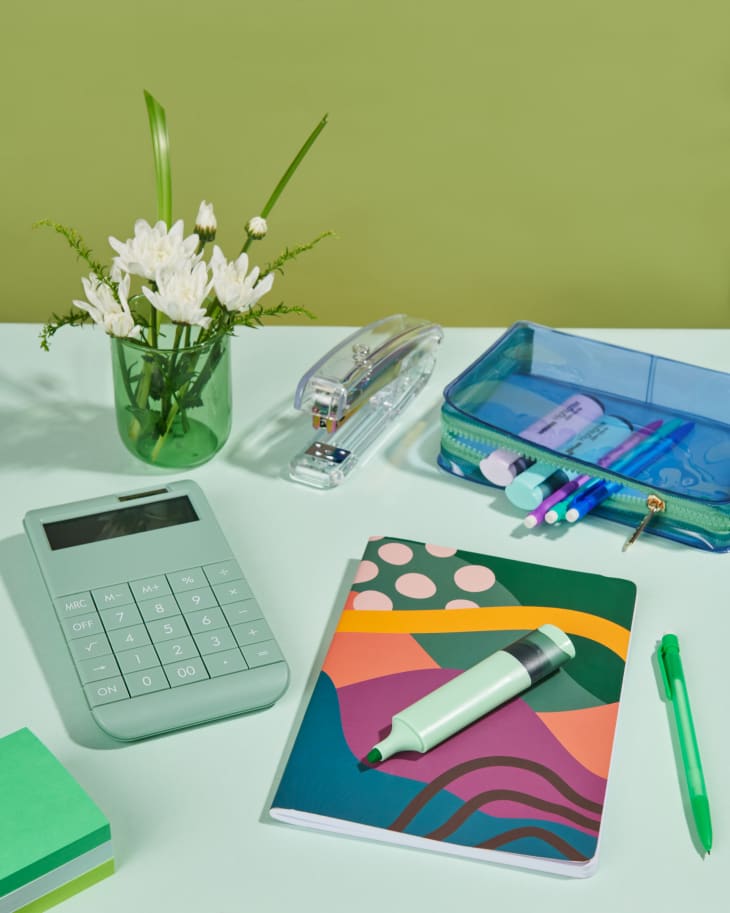 Desk with green calculator, notebook, pencil pouch, and small vase of flowers