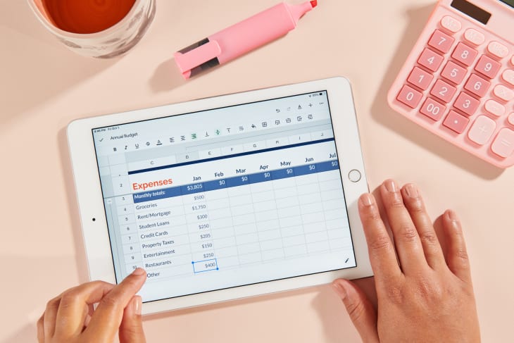 在iPad上用粉色背景、计算器和杯子将费用输入预算电子表格