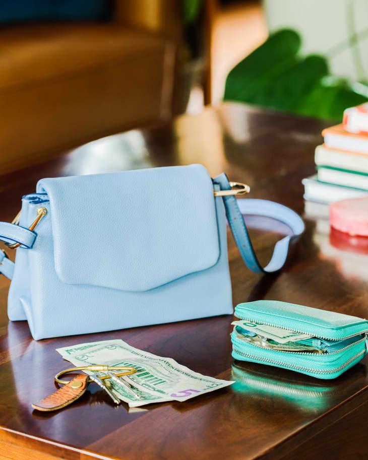 Blue purse, green wallet, some cash and keys on a coffee table
