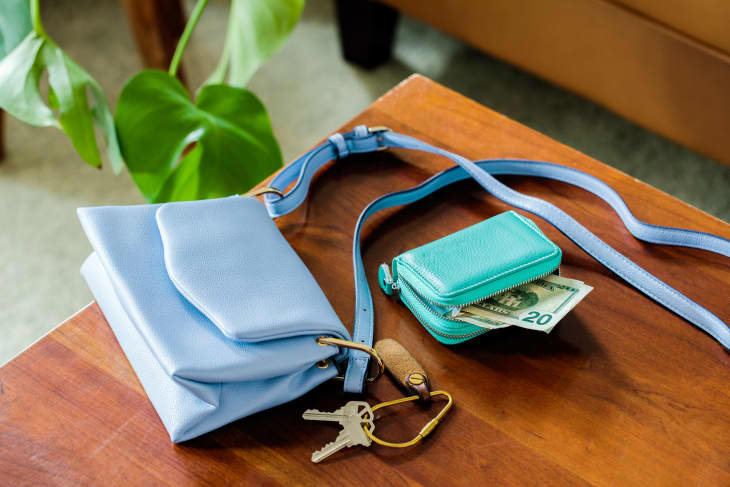 Blue purse, green wallet with some cash sticking out, and keys on a dining room table