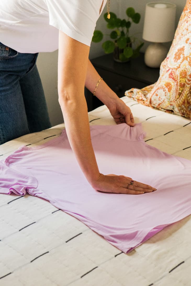 One step showing a woman folding a lavender t-shirt on bed