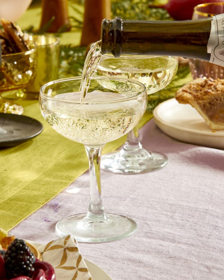 Close up view of champagne being poured into one of four coupe glasses on a white dish - on a colorful holiday tablescape.