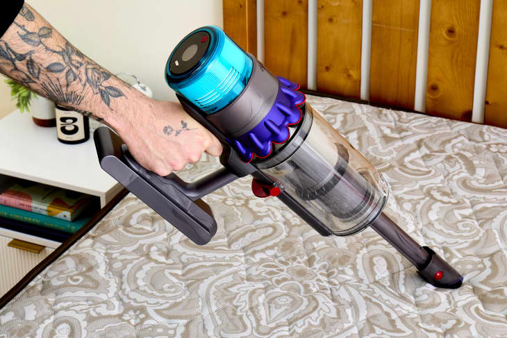 A person vacuuming a bare mattress