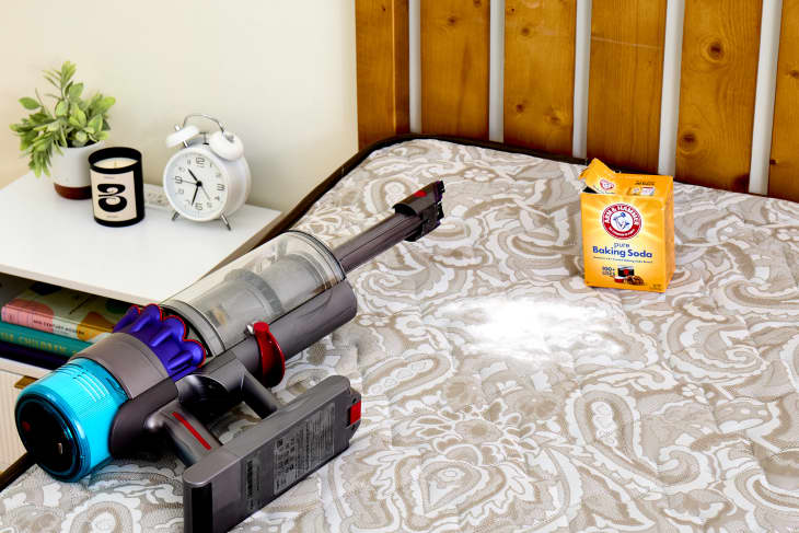 A handheld vacuum and baking soda on a bare mattress
