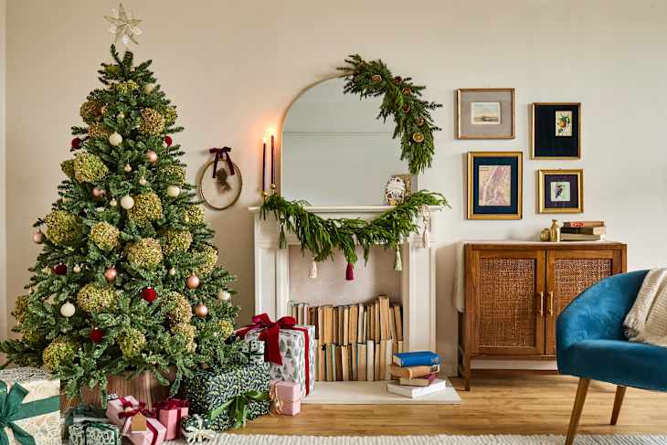 A decorated Christmas tree with gifts underneath, a fireplace adorned with greenery, and framed art on the wall.
