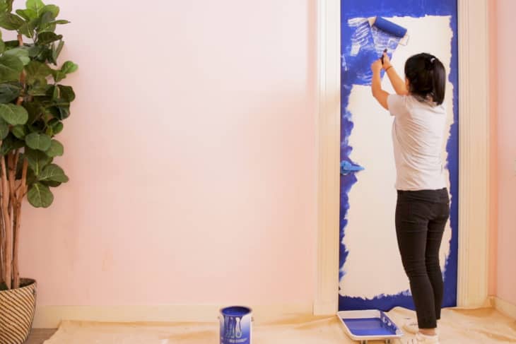 Woman rolls blue paint onto a white door