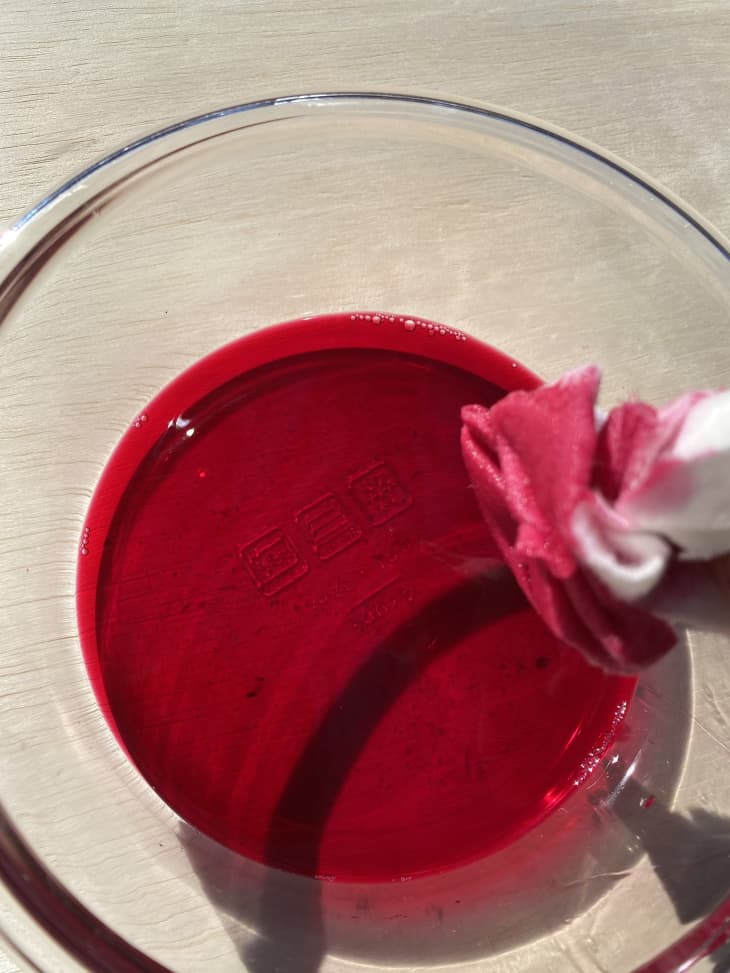 white cloth dipping into glass bowl full of beet juice