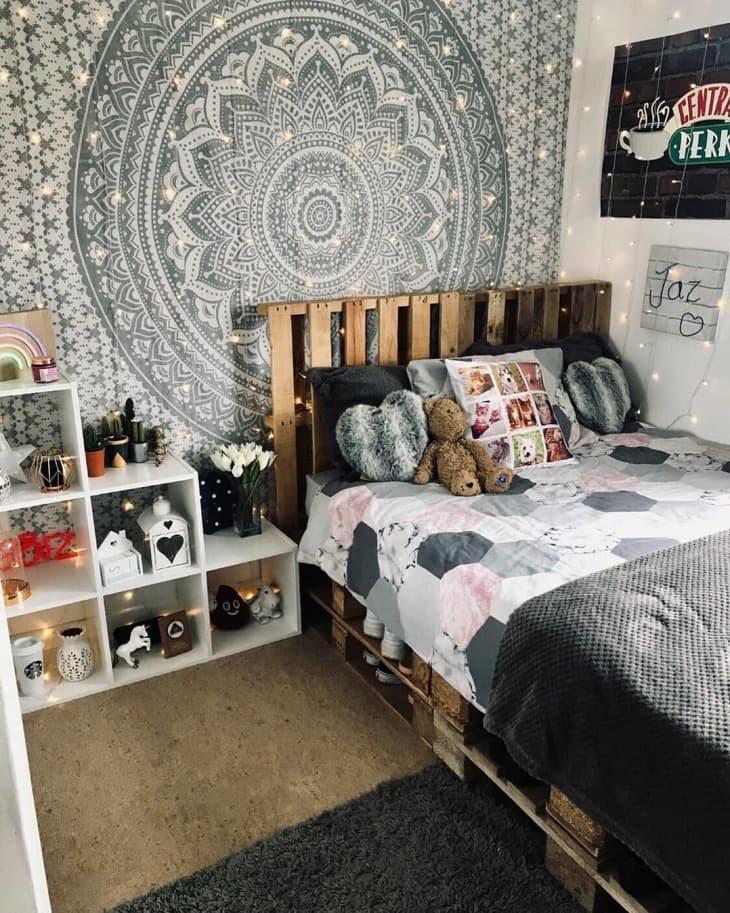 Pallet bed with headboard against a patterned wall hanging, with cube shelving next to it