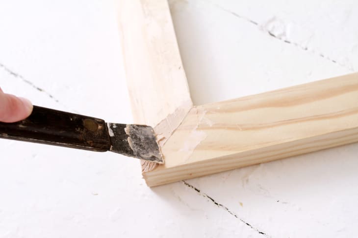 using a putty knife to apply wood filler to gaps in the wood picture frame