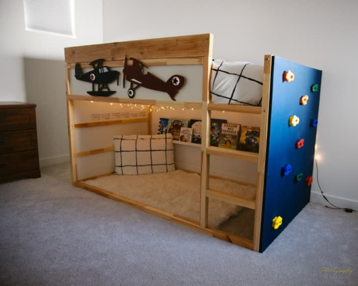 bunk bed with string lights underneath and a climbing wall on one side